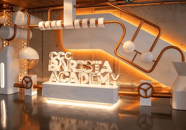 Illuminated "CCC BARISTA ACADEMY" sign integrated into a white and copper coffee-themed industrial display.